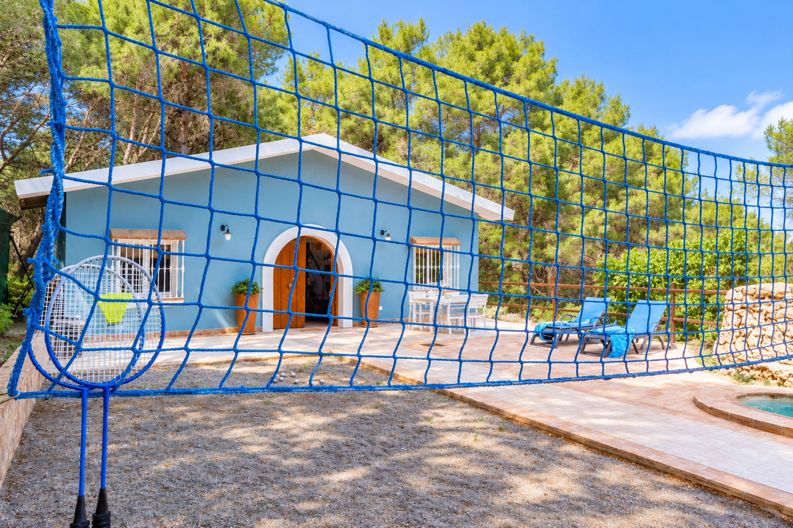 Una casa azul con la puerta abierta, un patio con sillas y una zona de piscina.