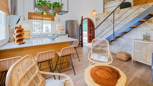 A modern kitchen with a central island, bar stools, and a staircase leading to an upper level.