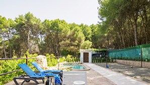 A wooden deck with a pool, lounge chairs, and a small building, surrounded by trees.