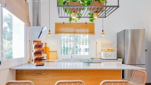 A modern kitchen with a central island, stainless steel appliances, wicker chairs, and a window with a view.