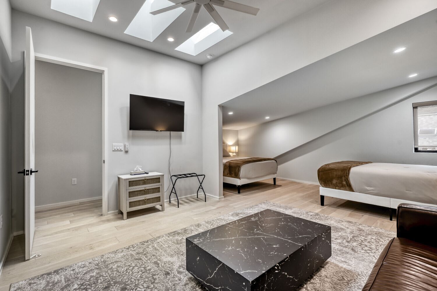 Ett modernt sovrum i loftstil med ett sluttande tak, en platt-TV, en säng, en soffa och ett soffbord i marmor.