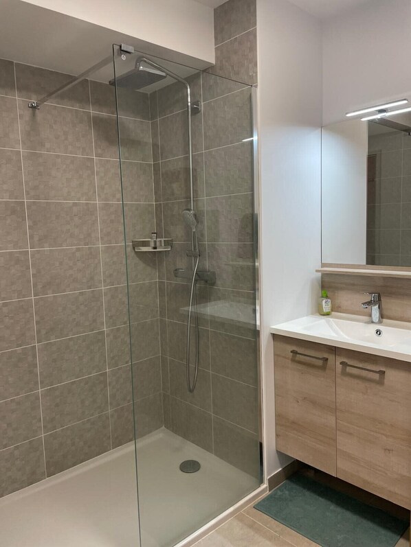 A modern bathroom with a glass-enclosed shower, a wooden vanity with a mirror, and a tiled floor.