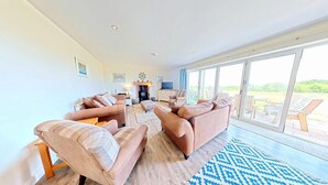 A spacious living room with a fireplace, sofas, and a large sliding glass door leading to an outdoor area.