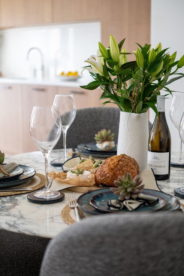 Una mesa de comedor dispuesta con platos, vasos, una botella de vino y una planta en maceta.
