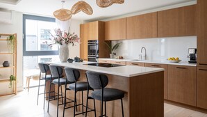 Una cocina moderna con una isla grande, taburetes de bar, armarios de madera y luces colgantes.