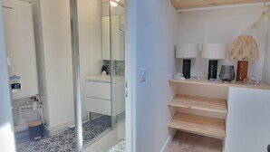 A bathroom with a glass shower enclosure, a toilet, and a sink. There are two wall-mounted lamps and a wooden shelf with decorative items.