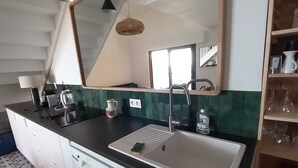 A modern bathroom with a large mirror, a sink, and a countertop with a coffee maker and a bottle of hand soap.