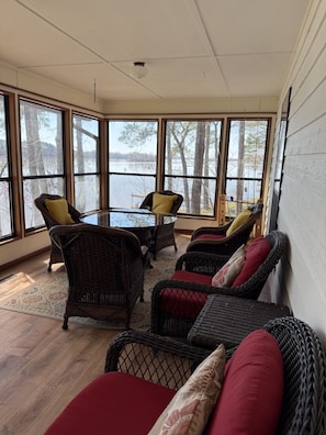 Una habitación con muebles de mimbre, una mesa de vidrio y grandes ventanales con vistas al agua.