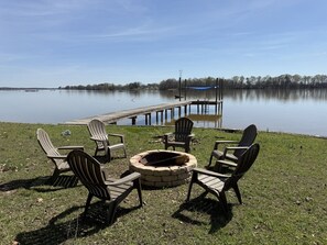 Eine Uferlandschaft mit Steg, Feuerstelle und Adirondack-Stühlen.