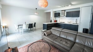 Una sala moderna con un sofá de cuero, un comedor con mesa y sillas, y una cocina con armarios oscuros y encimera blanca.