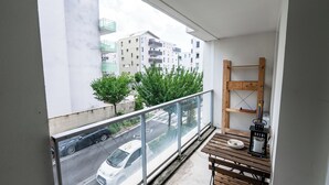 Un balcón con vista a una calle, una mesa con un cuenco y una botella, y un estante de madera.