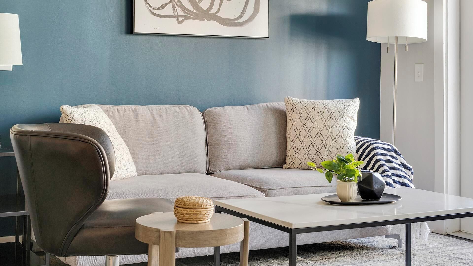 A modern living room with a grey sofa, a round wooden coffee table, and a black leather armchair.