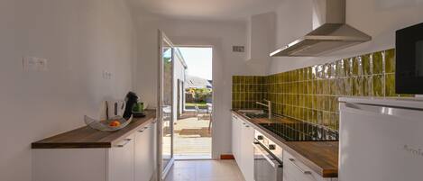 A narrow kitchen with white cabinets, a wooden countertop, and a green-tiled backsplash.