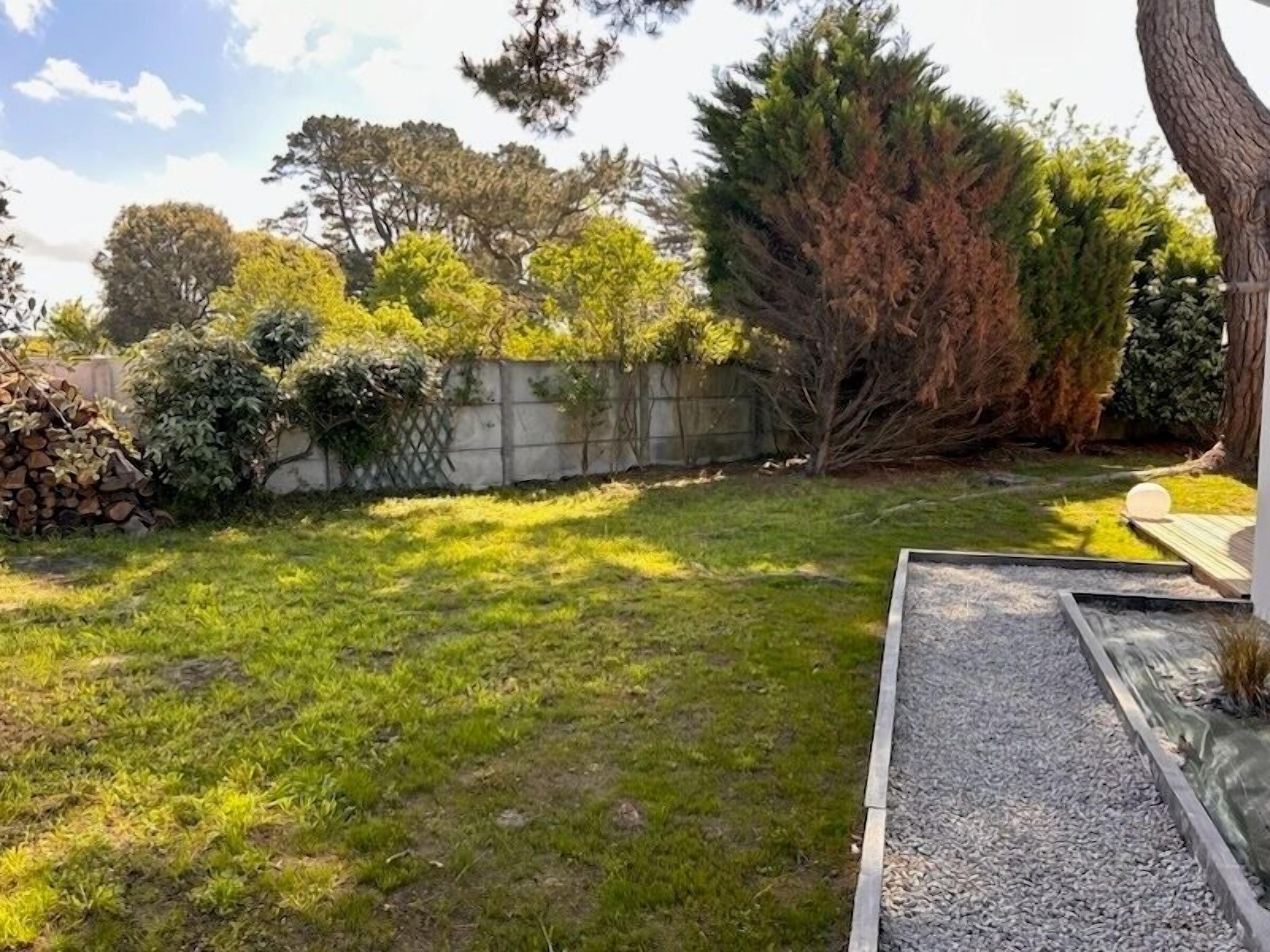 Un patio trasero con césped, un muro de piedra y diversas arboledas y arbustos.
