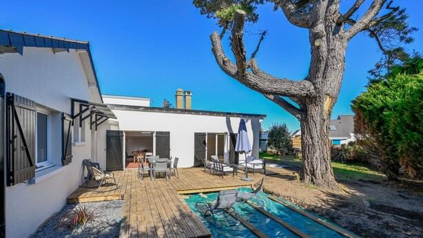 Ein modernes Haus mit einer Holzdiege, einem Schwimmbad und einem großen Baum.