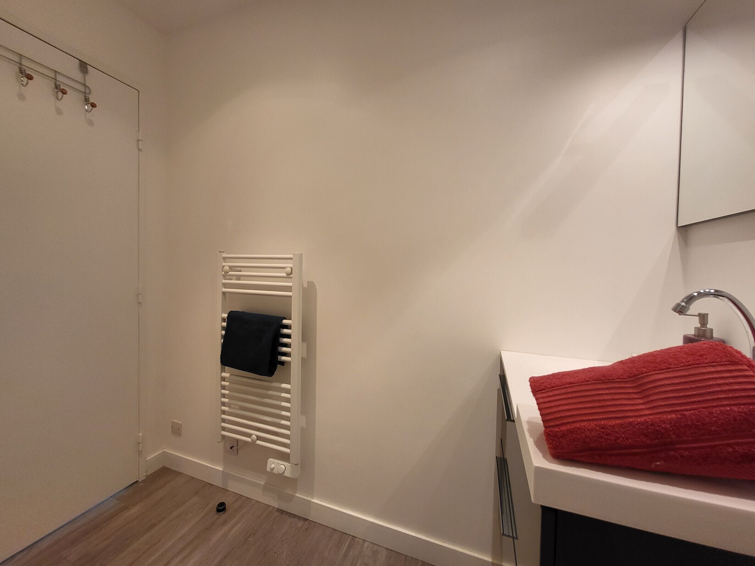 A bathroom with a white sink, a red towel, and a white towel warmer.