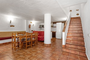 A dining area with a wooden table and chairs, a red sofa, and a staircase leading to an upper level.