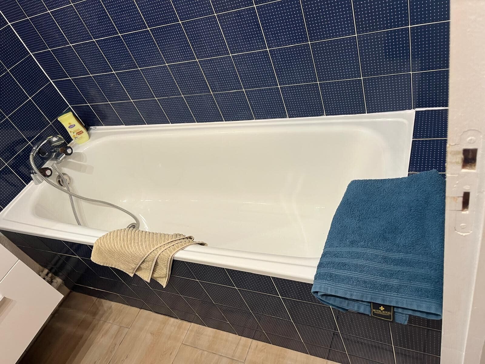 A bathroom with a white bathtub, a beige towel, and a blue towel on a rack.