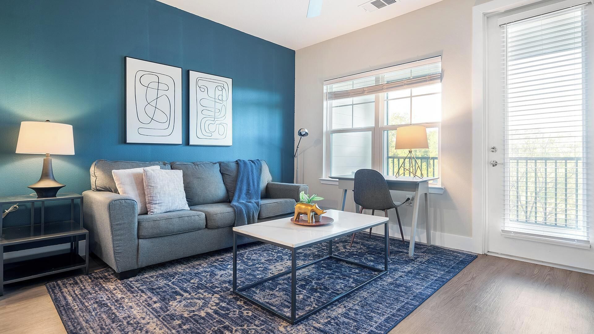 Un salon avec un canapé gris, une table basse, un tapis bleu et des œuvres d’art accrochées au mur.