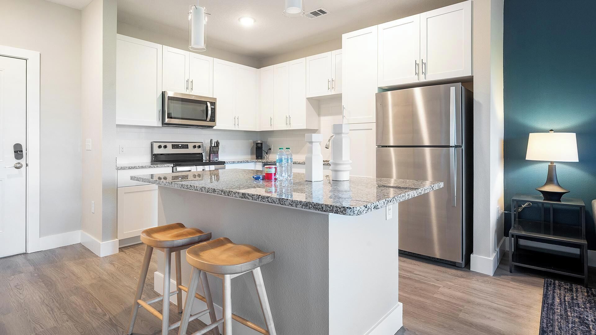 A modern kitchen with white cabinets, stainless steel appliances, a granite countertop, and wooden bar stools.