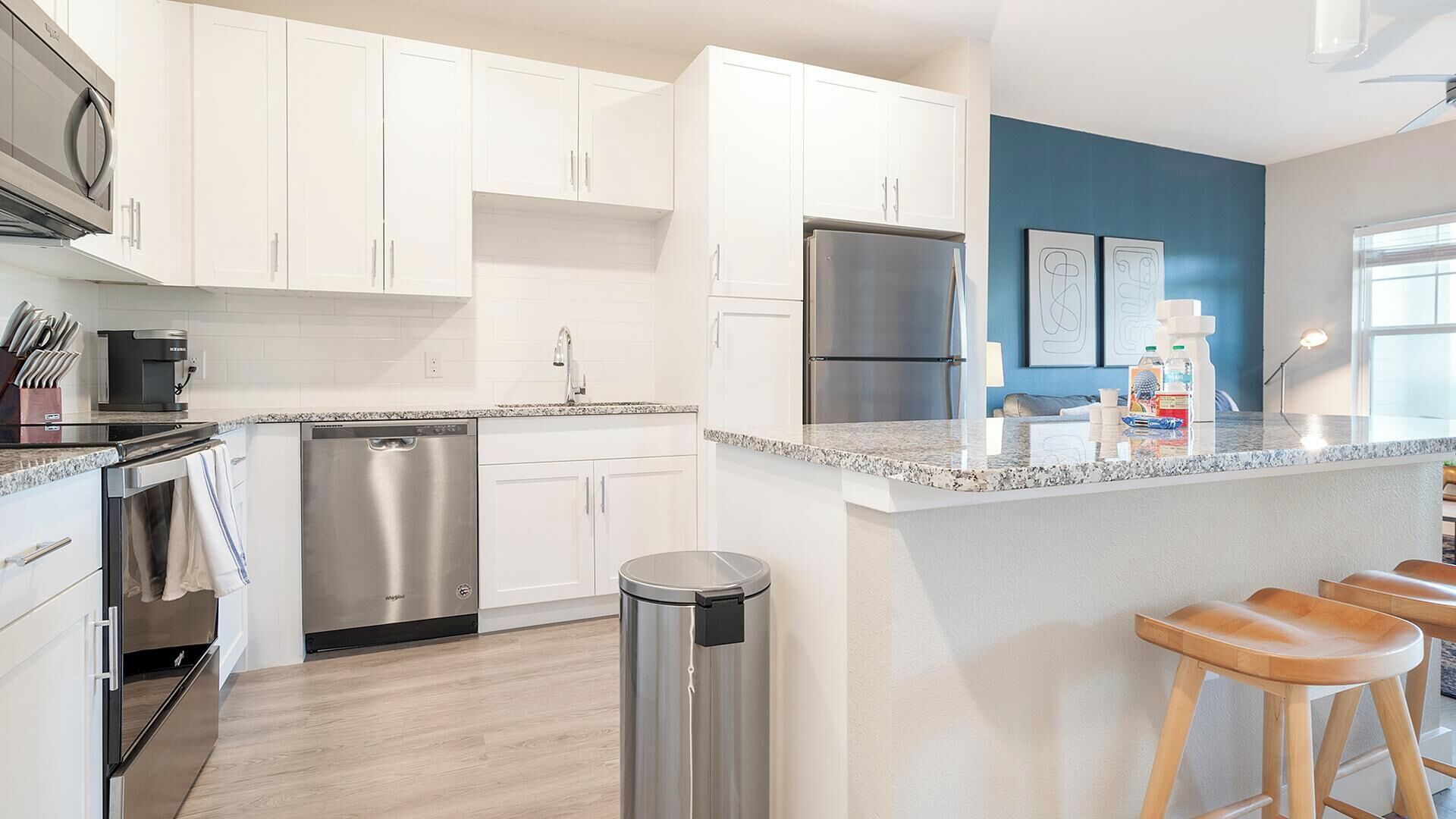 A modern kitchen with white cabinets, stainless steel appliances, a granite countertop, and a blue accent wall.
