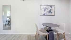 Zona pranzo con tavolo rotondo e due sedie, un grande specchio e un’opera d'arte astratta incorniciata a parete.