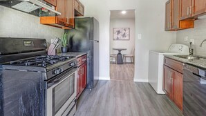 A kitchen with a stove, oven, refrigerator, and sink. There is a dining table and chairs in the adjacent dining area.