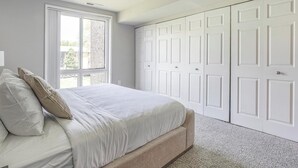 A bedroom with a bed, a large window, and a set of white doors.