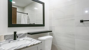 Un baño moderno con un lavamanos de mármol, un grifo negro, un inodoro blanco y un espejo grande.