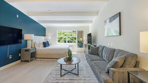 A modern hotel room with a bed, a sofa, a coffee table, and a TV. - Landing | Amazing Studio, Pool, Gym (Raleigh)
