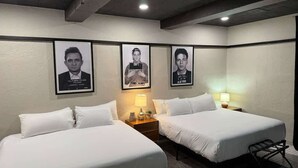 Una habitación de hotel con dos camas, una mesita de noche con lámpara y tres carteles enmarcados en la pared.