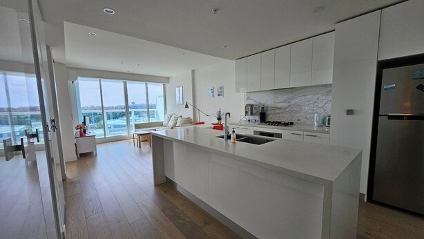 A modern kitchen with a large island, white cabinetry, and a view of the city.