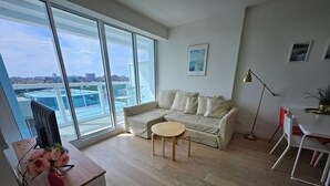 A modern living room with a large sliding glass door, a sofa, a small round table, and a TV on a wooden stand.