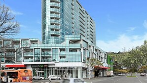A modern hotel with a curved glass facade, a Woolworths store, and a Woolworths sign.