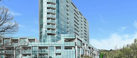 A modern hotel with a curved facade, multiple balconies, and a Woolworths store at the ground level.