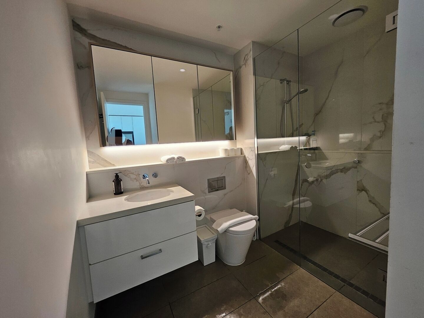 Un baño moderno con tocador de mármol, cabina de ducha de vidrio y un espejo grande.