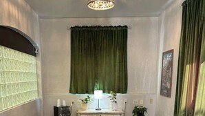 A living room with a chandelier, green curtains, a patterned rug, and a wooden coffee table. - The Block Basic Room - Queen (Bisbee)