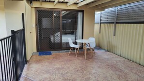 A balcony with a sliding glass door leading to a bedroom, a small round table with two chairs, and a blue welcome mat. - Comfortable Studio Granny Flat Mermaid Water (Mermaid Waters)