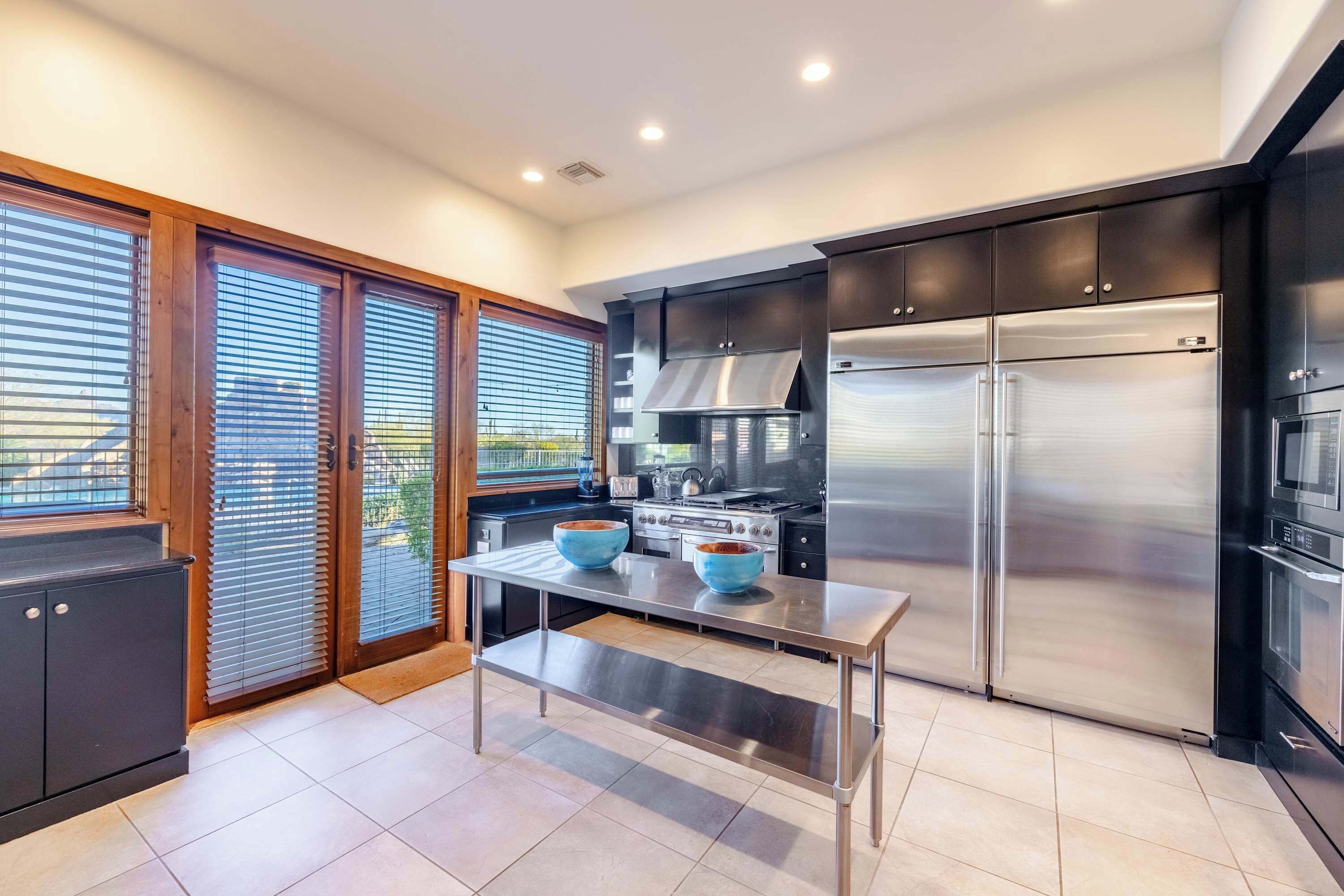 A modern kitchen with a stainless steel refrigerator, a stove, and a dining table with two blue bowls.