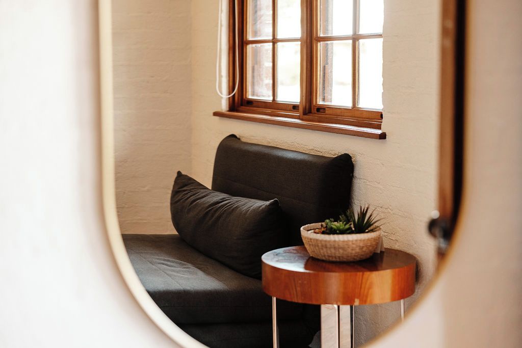 A cozy corner with a dark leather sofa, a small wooden side table with a plant, and a window with wooden frames.