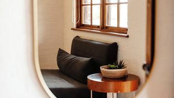 A cozy corner with a dark leather sofa, a small wooden side table with a plant, and a window with wooden frames.