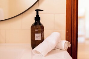 A bathroom with a bottle of Ashley & Co. hand soap and a rolled white towel on a white countertop. - The Retreat at Wisemans (Sydney)