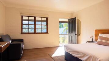 A bedroom with a bed, a desk, a chair, a window, and a door leading outside.