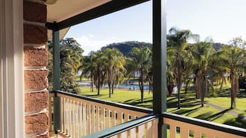A balcony with a view of a well-maintained lawn and palm trees, a brick wall on one side, and a clear sky.