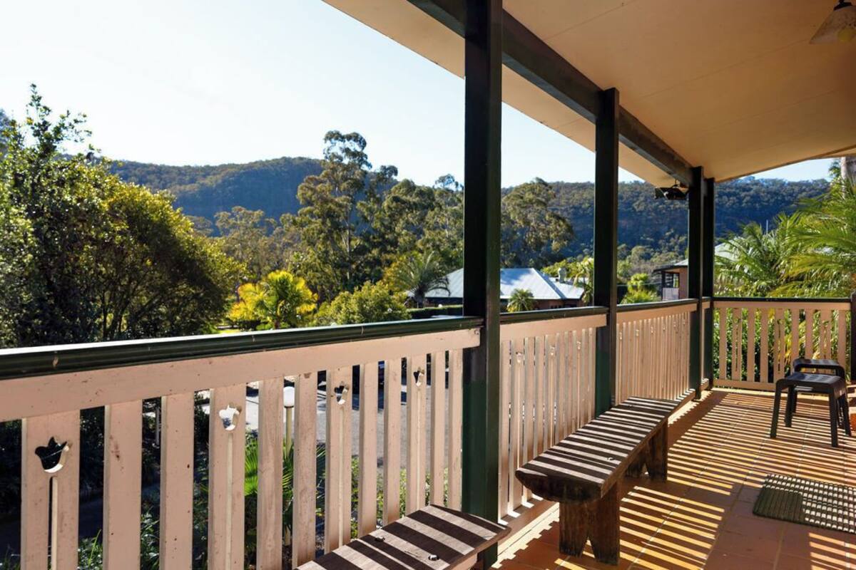 A covered outdoor area with a wooden bench and a table, overlooking a hilly landscape with trees and a building in the distance.
