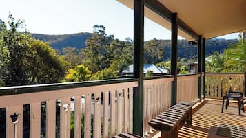 A covered outdoor area with a wooden bench and a table, overlooking a hilly landscape with trees and a building in the distance.