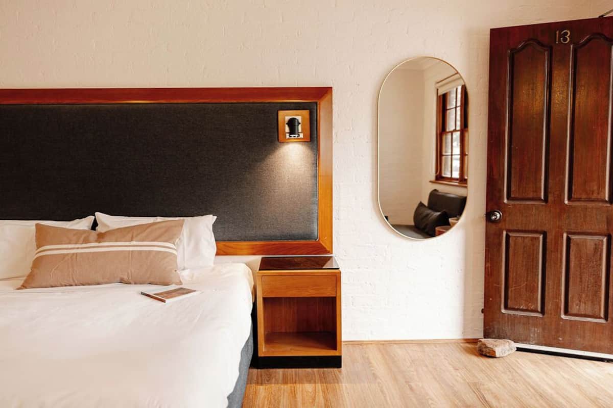 A neatly made bed with a wooden headboard, a bedside table, and a mirror on the wall.