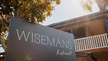 A sign for Wisemans Retreat with a balcony and brick building in the background.