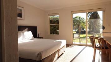 A bedroom with a large bed, a desk, and a view of a garden through a sliding glass door.