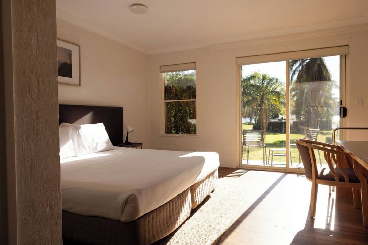 A bedroom with a large bed, a desk, and a view of a garden through a sliding glass door.
